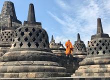 An orange-robed monk standing among the stupas of Borobudur.