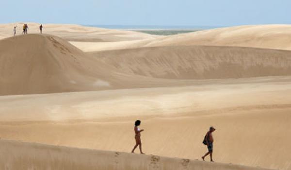 Swirls of white sand flow across the dunes, dwarfing hikers in Lençóis Maranhens