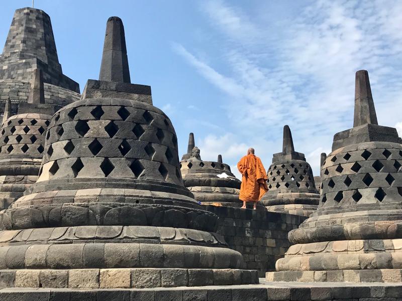 An orange-robed monk standing among the stupas of Borobudur.